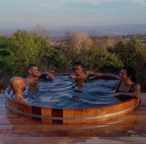 Group enjoying a cedar hot tub with panoramic Hudson Valley views at golden hour