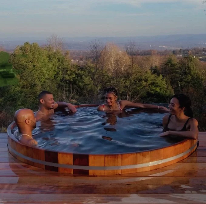 Group of friends in a cedar hot tub with panoramic Hudson Valley views at golden hour