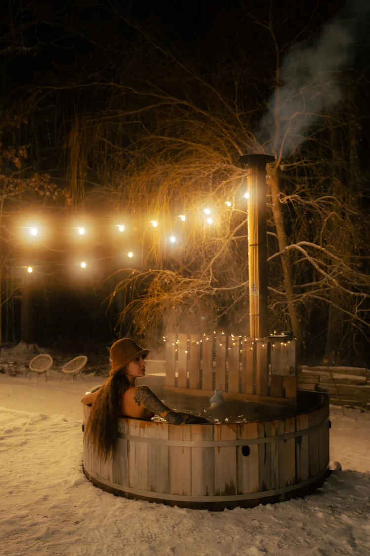 Cedar hot tub in winter snow with string lights and steam rising at night