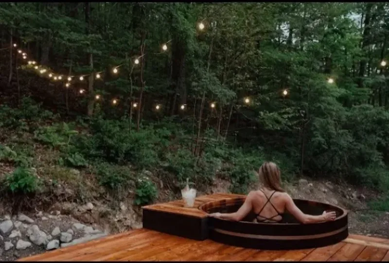 Cedar hot tub lit by string lights in a Hudson Valley forest at dusk