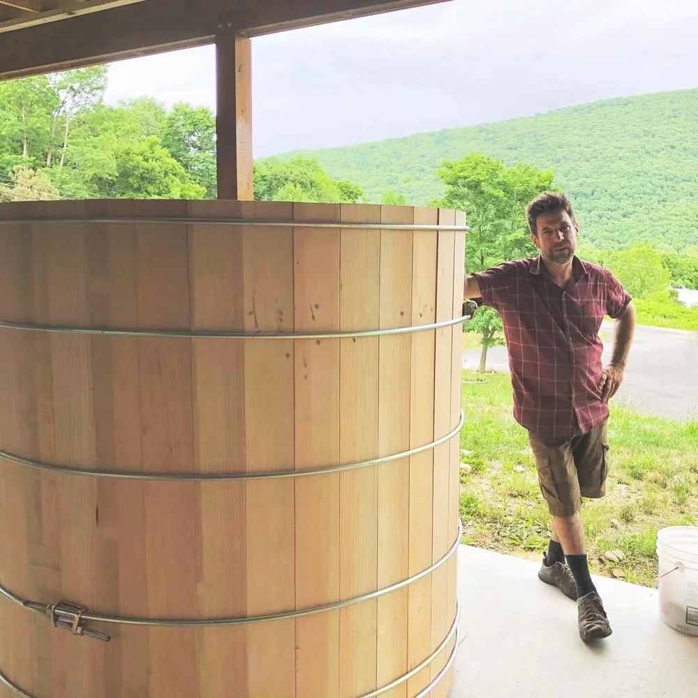 John Cox, founder of Hudson Valley Hot Tubs, beside a freshly built cedar hot tub with Catskill Mountains in the background