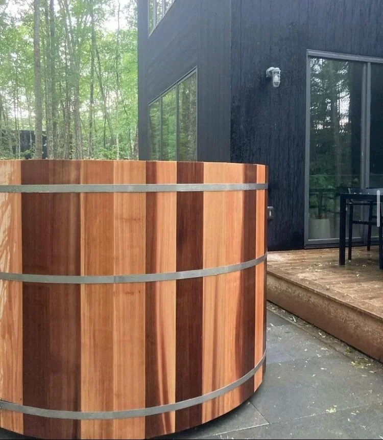 Shou sugi ban charred black cedar hot tub beside a modern black house in Hudson Valley woods